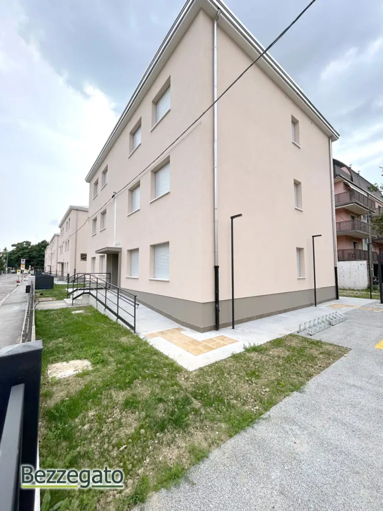 CASA ROSA copia_web | Bezzegato Three-story beige residential building with a ramp, path, and street lamps in a neighborhood.