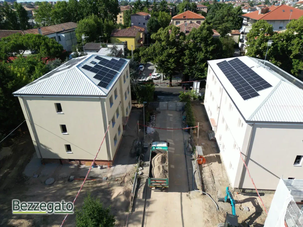 DJI_0514_web | Bezzegato Aerial view of a construction site between two beige buildings with solar panels on their sloped roofs; a truck and equipment on the road below.