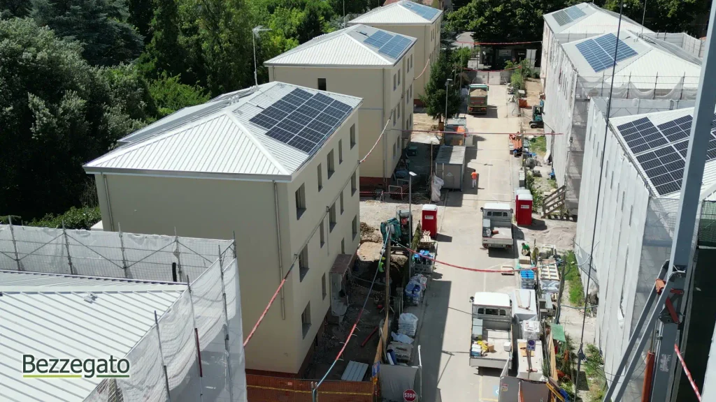 vlcsnap-2026-10-28-18h42m42s830_web | Bezzegato Aerial view of a construction site with beige buildings and solar panels on the rooftops, a narrow street with trucks and equipment nearby.