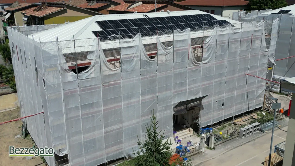 vlcsnap-2026-10-28-18h43m12s850_web | Bezzegato Building under construction wrapped in white protective netting, with solar panels on the roof