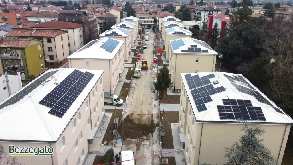 vlcsnap-2026-10-28-18h43m32s911_web | Bezzegato Aerial view of a residential street under construction between beige apartment buildings with solar panels on the roofs.